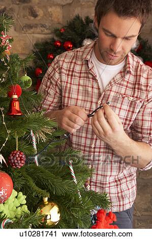 Stock Image - Young man fixing Christmas tree lights. Fotosearch