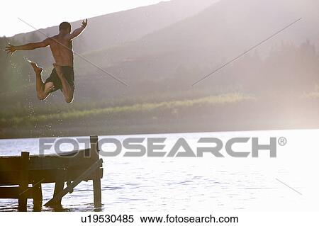 Stock Photography - Young man jumping into lake. Fotosearch
