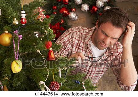 Picture - Young man trying to fix Christmas tree lights. Fotosearch