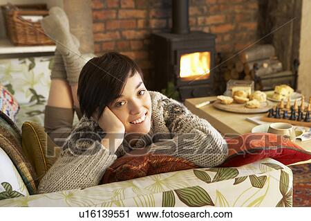 Stock Image - Young woman relaxing by fire. Fotosearch