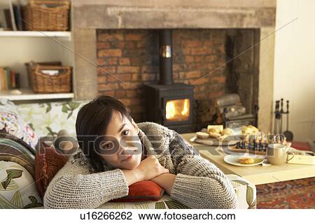 Stock Image - Young woman relaxing by fire. Fotosearch