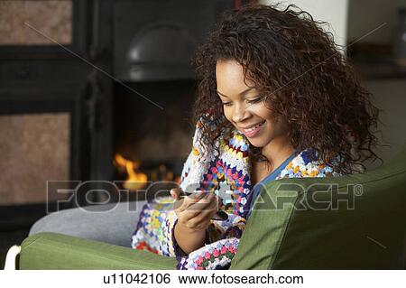Stock Photograph - Young woman sitting by fire with phone. Fotosearch
