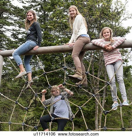 Stock Photograph - Four female friends on rope spider web in a park, Bergen, Norway. Fotosearch