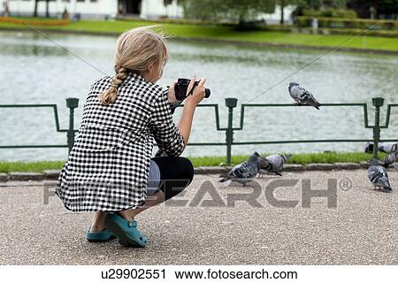 Stock Image - Girl taking picture of pigeons with a camera, Bergen, Norway. Fotosearch