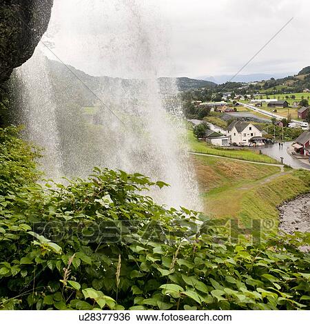 Stock Photograph - Waterfall with a village in the background, Steinsdalsfossen, Norheimsund, Hardangervidda, Hardanger, Norway. Fotosearch
