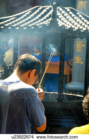Picture - Rear view of a man holding incense sticks. Fotosearch