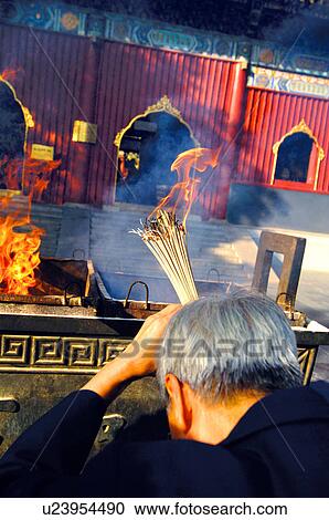Stock Image - Rear view of a man holding incense sticks. Fotosearch