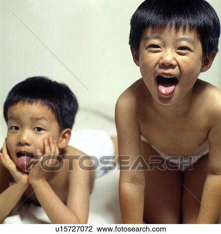 Stock Image - Two brothers sticking their tongues out on the bed. Fotosearch