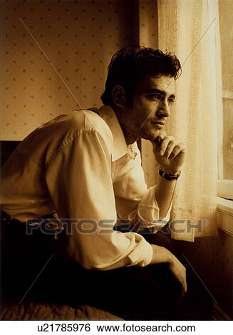 Stock Photograph - Close-up of a young man sitting on the bed and thinking. Fotosearch