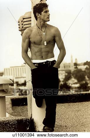 Picture - Bare chested young man leaning against a column with his hands in pockets. Fotosearch