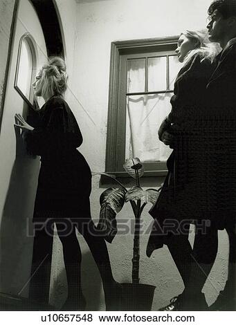 Woman peeking through a door window with her friends standing behind her View Large Photo Image Stock Photo - Woman peeking through a door window with her friends standing behind her. Fotosearch