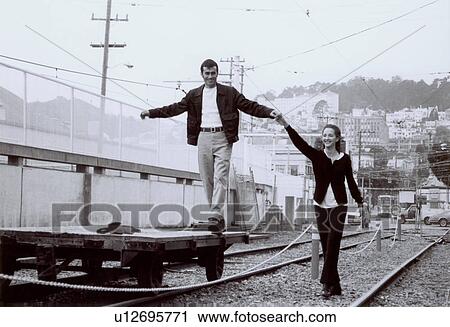 Young man standing on a trolley and holding hands of a young woman on a railroad track View Large Photo Image Stock Image - Young man standing on a trolley and holding hands of a young woman on a railroad track. Fotosearch