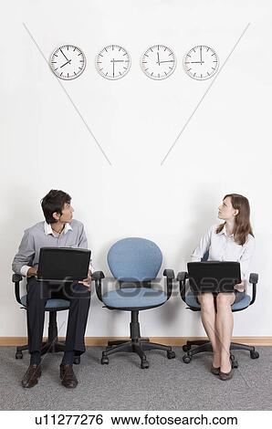 Stock Photograph - Business people sitting with laptop and looking up for the time together. Fotosearch