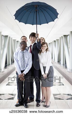 Business people standing under an umbrella and smiling View Large Photo Image Stock Photo - Business people standing under an umbrella and smiling. Fotosearch