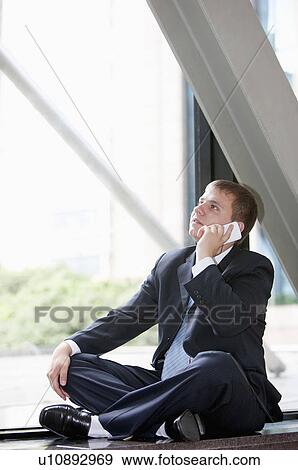 Stock Photo - Businessman sitting, using mobile phone and looking up. Fotosearch