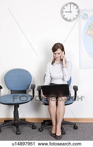Businesswoman sitting on chair with laptop and holding mobile phone View Large Photo Image Stock Image - Businesswoman sitting on chair with laptop and holding mobile phone. Fotosearch