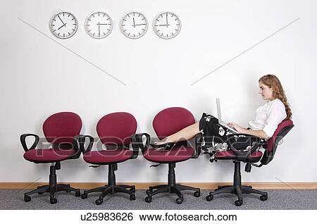 Stock Photograph - Businesswoman sitting with legs on chairs and using laptop. Fotosearch