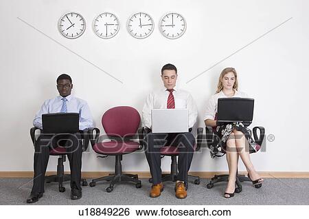 Stock Photograph - Three business people sitting on chairs with laptop at 9 o'clock. Fotosearch