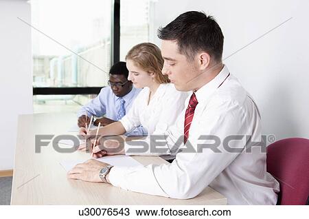Stock Image - Three business people sitting together and writing notes. Fotosearch