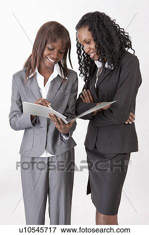 Stock Photo - Two businesswomen standing and discussing together with smile. Fotosearch
