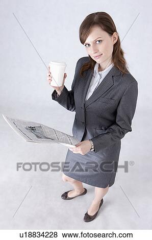 Stock Photo - Businesswoman holding a cup and newspaper and looking up. Fotosearch