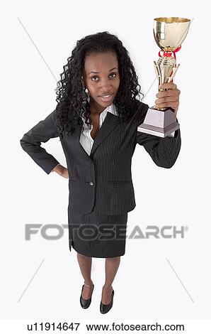 Stock Photo - Businesswoman holding a trophy and looking up. Fotosearch