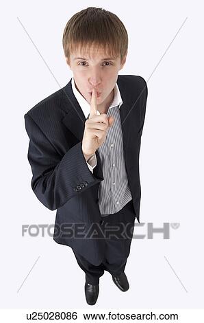 Stock Photograph - Young businessman looking up and putting finger on lips. Fotosearch