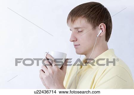 Picture - Young man listening music and holding a cup with eyes closed. Fotosearch