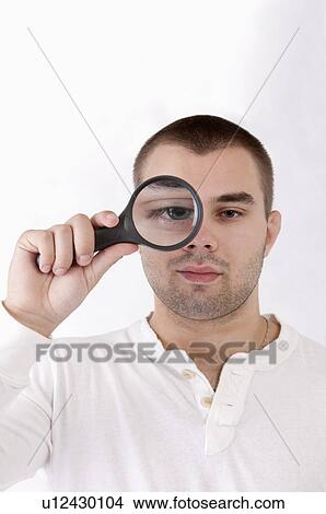 Young man putting a magnifying glass on one eye View Large Photo Image Picture - Young man putting a magnifying glass on one eye. Fotosearch