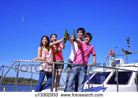 Stock Image - Four people standing in cruise ship and celebrate with beer together. Fotosearch