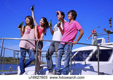 Stock Image - Four people standing on the cruise ship and holding beer together. Fotosearch