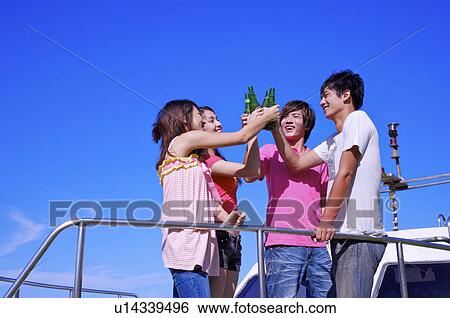 Stock Photograph - Four people standing on the cruise ship and celebrating with beer. Fotosearch