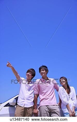 Stock Image - Three people standing together near the car and looking away. Fotosearch