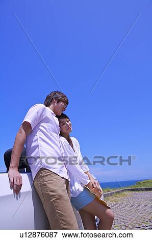 Young couple leaning on the car together and smiling View Large Photo Image Stock Photo - Young couple leaning on the car together and smiling. Fotosearch