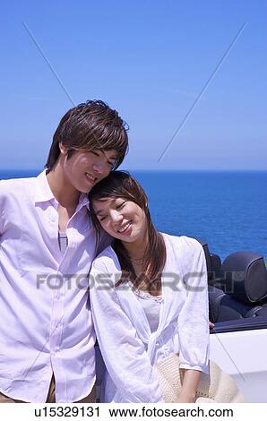 Stock Image - Young couple leaning together and smiling happily. Fotosearch
