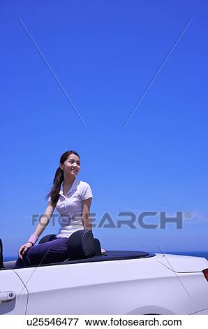 Stock Photo - Young woman sitting in the car and looking away with smile. Fotosearch