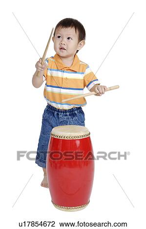 Stock Image - Little boy playing drum and looking away. Fotosearch