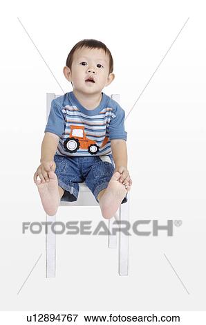 Stock Photo - Little boy sitting on chair with mouth open and looking at the camera. Fotosearch