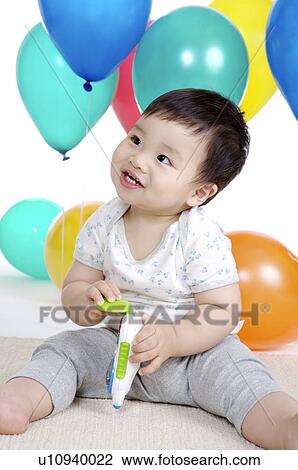 Stock Image - Little boy sitting, playing a toy and looking up with smile. Fotosearch