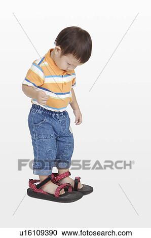 Stock Image - Little boy wearing a pair of big shoes and looking down. Fotosearch
