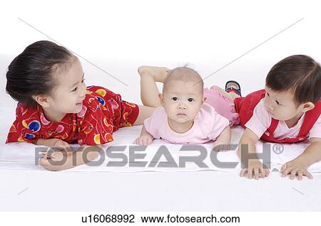 Stock Image - Three children lying on front in a row together. Fotosearch