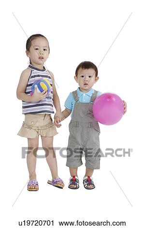 Stock Image - Two children holding hands together and looking at the camera. Fotosearch