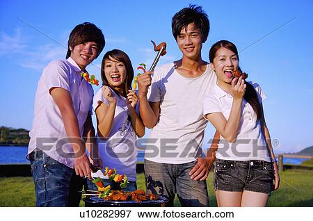 Stock Photo - Four people barbecuing outside and holding food together,. Fotosearch