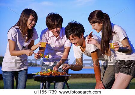 Stock Photo - Four people having barbecue outside together and smiling happily,. Fotosearch