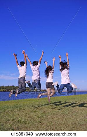 Four people jumping in mid-air with arms outstretched, View Large Photo Image Stock Photo - Four people jumping in mid-air with arms outstretched,. Fotosearch