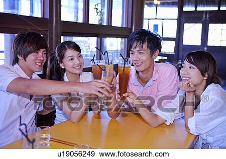 Stock Photo - Four people sitting together and holding drink with smile,. Fotosearch