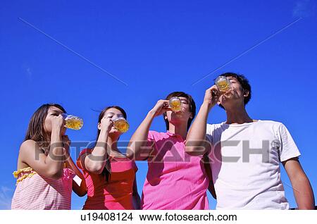 Picture - Four people standing and drinking beers together,. Fotosearch