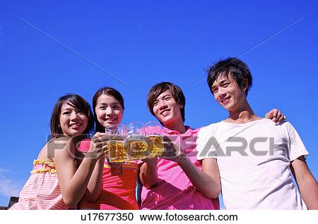 Stock Image - Four people standing and holding beers together,. Fotosearch