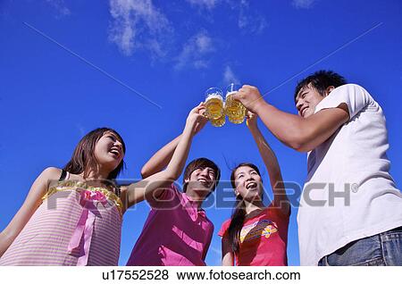 Stock Photo - Four people toasting with beer and smiling happily,. Fotosearch