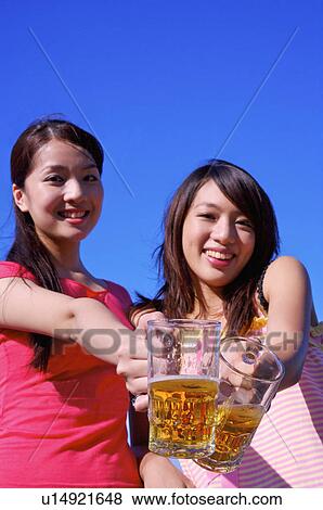 Stock Photo - Two women holding beers and smiling at the camera,. Fotosearch